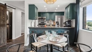 A modern kitchen with dark green cabinets, stainless steel appliances, and a round dining table with chairs. - The Southwestern Park City Mountain Resort Condo (Park City)