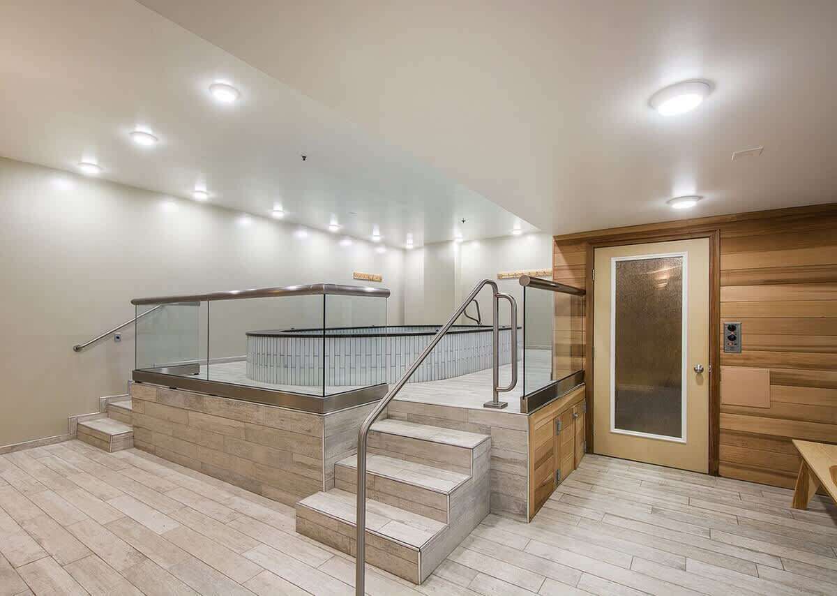 A modern interior with a staircase leading to a glass-enclosed area, wooden paneling on the walls, and a bench.