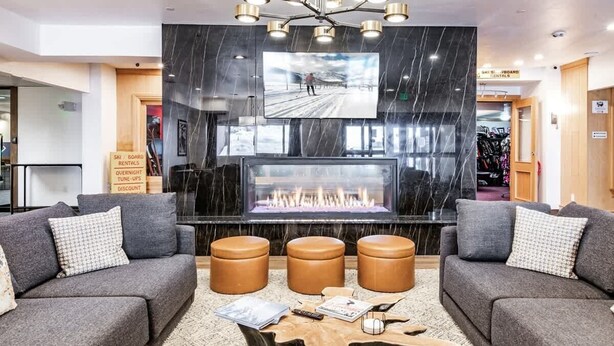 A modern lobby with a fireplace, leather sofas, a large TV screen, and a ski/board rental sign. - The Southwestern Park City Mountain Resort Condo (Park City)