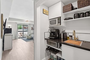 Una cocina compacta equipada con microondas, cafetera y espacio para guardar vino.