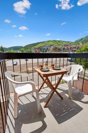 Un balcón con una mesa y sillas, vista a un pueblo y cielo despejado.