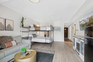 A modern, compact living space with a bunk bed, sofa, coffee table, and kitchen area.