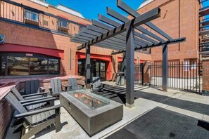 Ein Sitzbereich im Freien mit Adirondack-Stühlen und einem Feuerbereich, ein Ziegelgebäude mit roter Markise und eine Metall-Pergola.