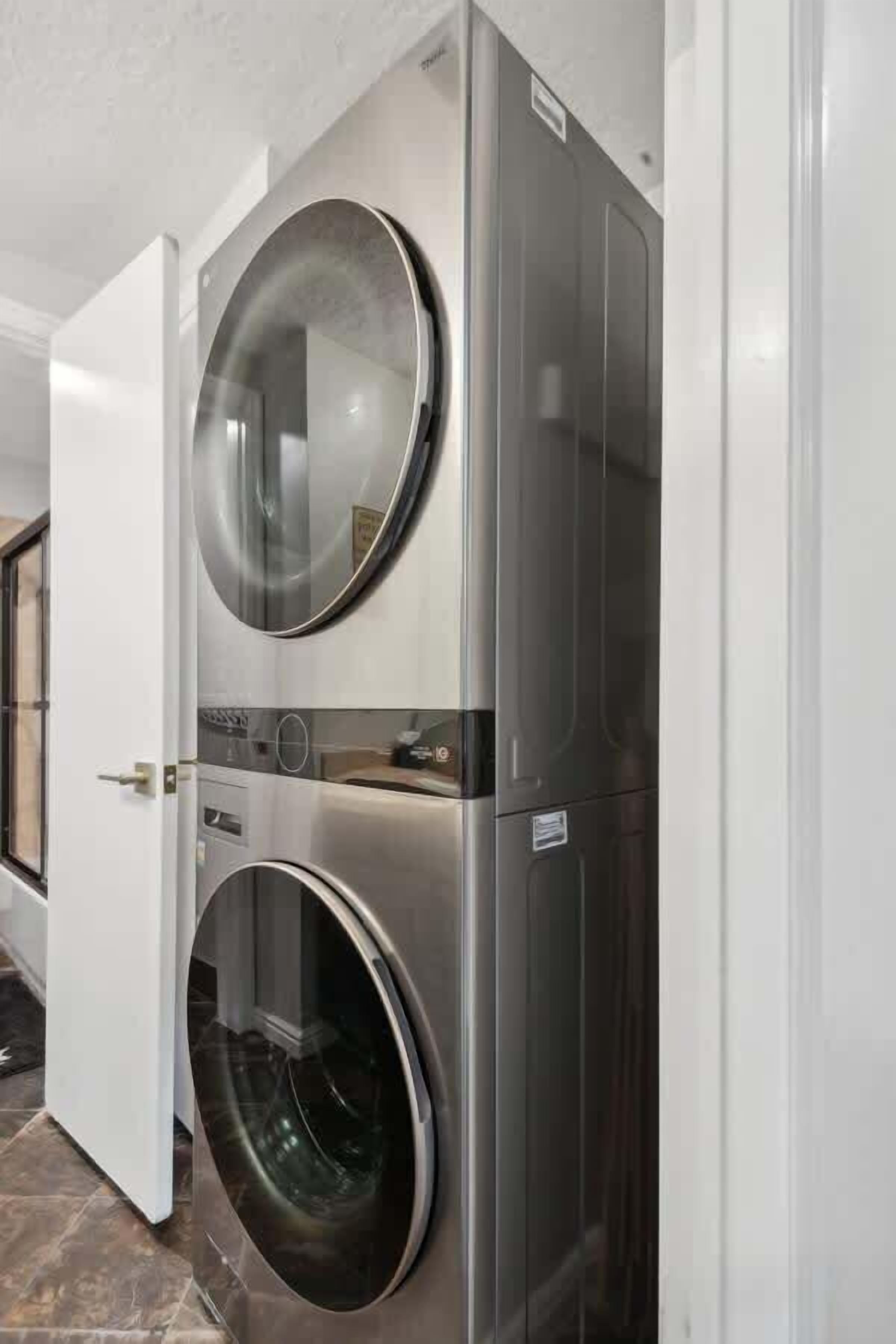 A stacked washer and dryer unit in a room with a white door and tiled floor.