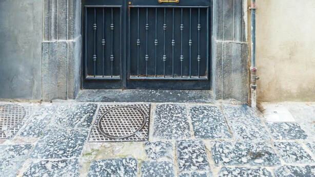 A black double door with a decorative metal arch above it, set in a building with a stone and concrete facade. - White Blue Apartment at Sanit by Wonderful Italy (Naples)