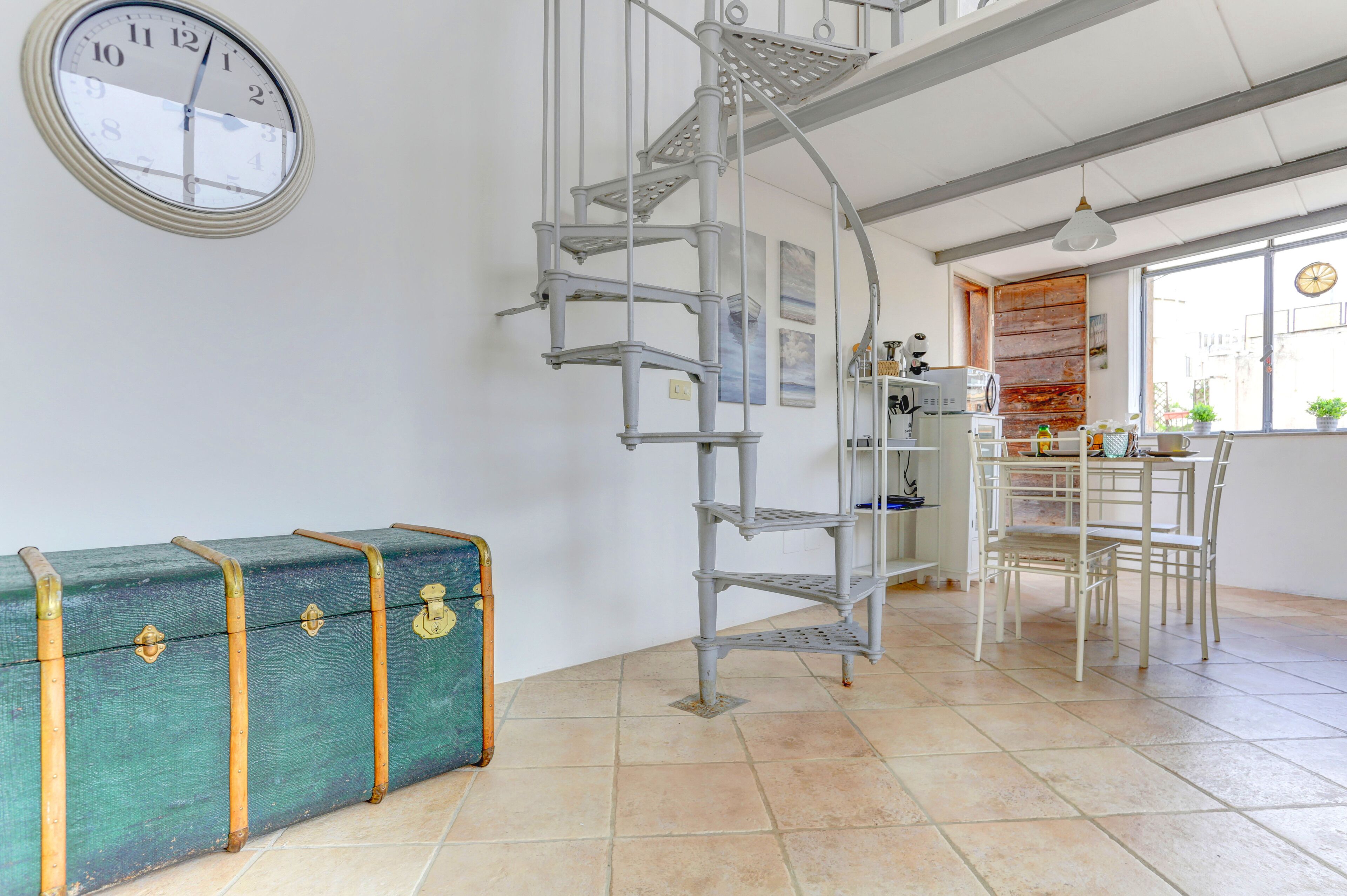 A spiral staircase, a green suitcase, a clock, and a dining area with chairs and a table.