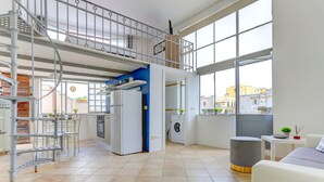 Una cuina moderna amb rentadora integrada, un entrepís amb barana i grans finestres que donen vista a la ciutat.