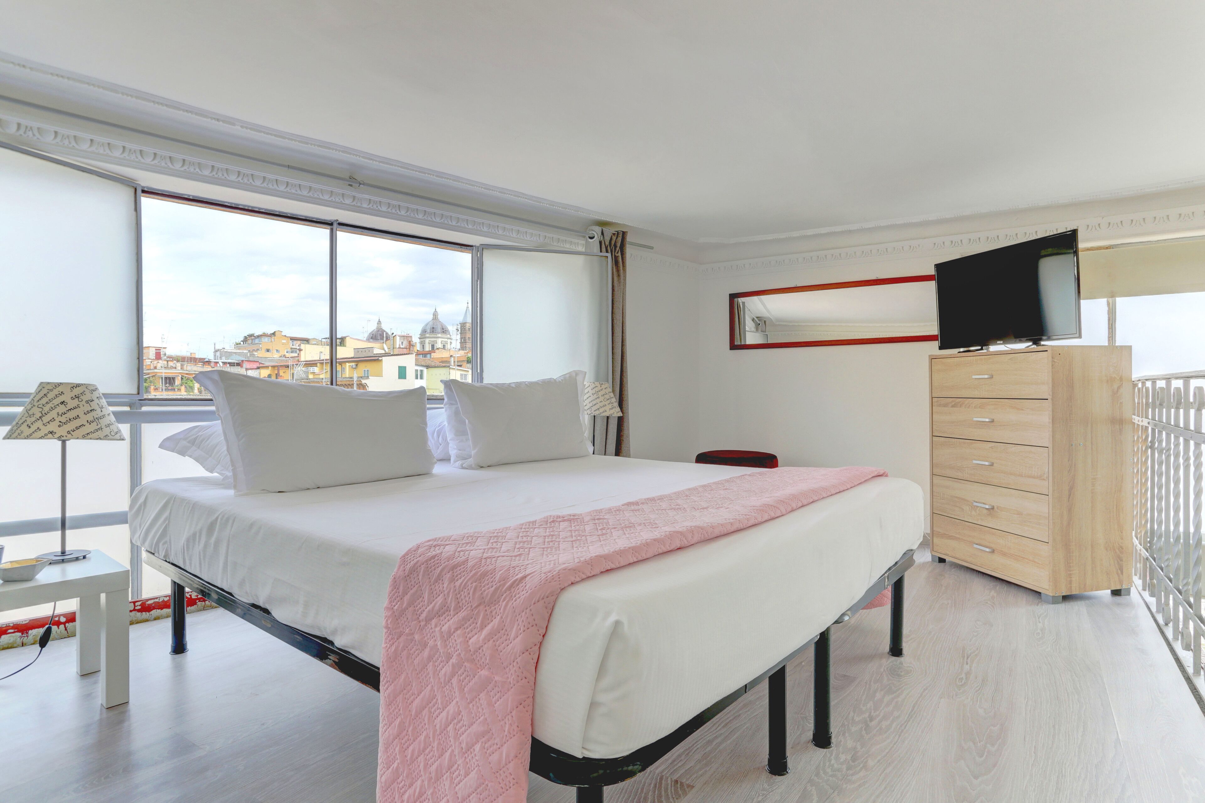 Ein Hotelzimmer mit einem großen Bett, einem Schminktisch, einem Fernseher und einem Balkon mit Blick auf die Stadt.