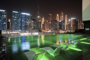 A rooftop pool with a city skyline in the background, including the DAMAC building. - Waves - Premium 1BR Apartment Overlooking Burj Khalifa (Dubai)
