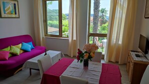 A room with a pink sofa, a small table with a vase of flowers, and a TV on a wooden cabinet. - Apartment and Room Bitinada (Rovinj)
