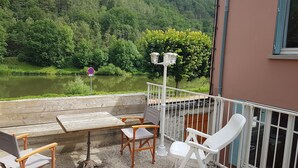 Een balkon met een tafel en stoelen, met uitzicht op een rivier, omgeven door groen.