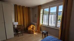 Een kamer met een bed, een stoel, een tafel, een radiator en een raam met gordijnen.