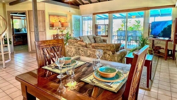 A dining area with a wooden table set for four, a sofa, and a TV in the background.