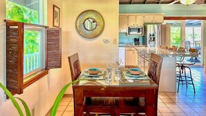 A dining area with a table set for four, a kitchen in the background, and a ceiling fan.