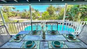 A dining table set for four with a view of a swimming pool and tropical vegetation.