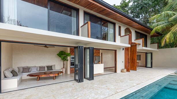 Une maison moderne à deux étages, dotée d’une piscine, de grandes fenêtres et d’une terrasse en bois.