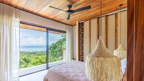 Une chambre avec une grande fenêtre, un ventilateur de plafond et un lit recouvert d’une couverture rose.