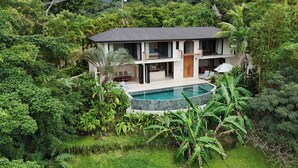 Une maison à deux étages avec une piscine, le tout entouré d’une végétation luxuriante.