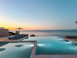 An infinity pool with lounge chairs and umbrellas, overlooking a body of water and distant mountains. - Sampatiki Suites - Seaview Luxury Suites With Breakfast And Spa (South Kynouria)