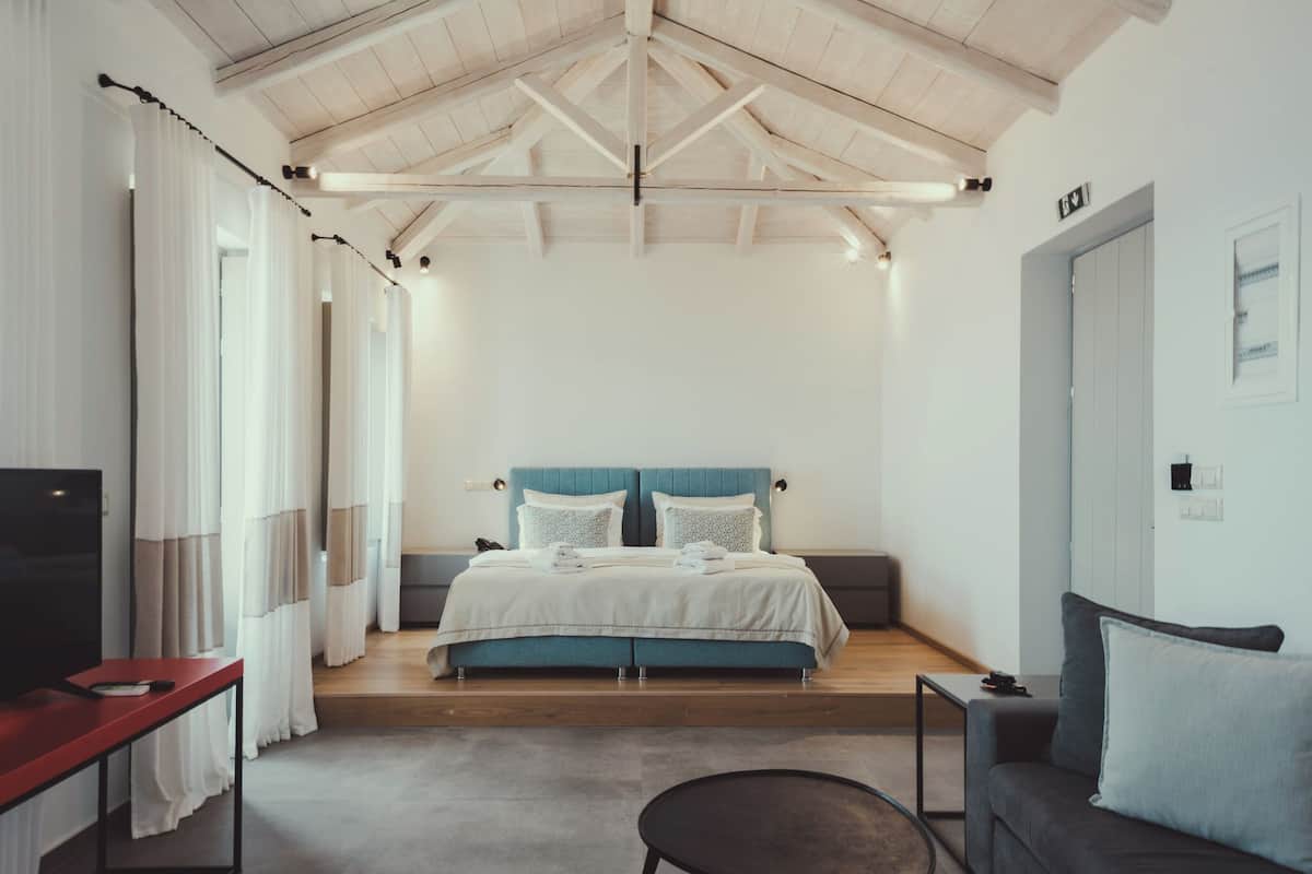 A bedroom with a bed, curtains, a TV, a sofa, and a ceiling with wooden beams.