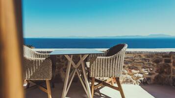 A table and two wicker chairs on a balcony overlooking the sea.