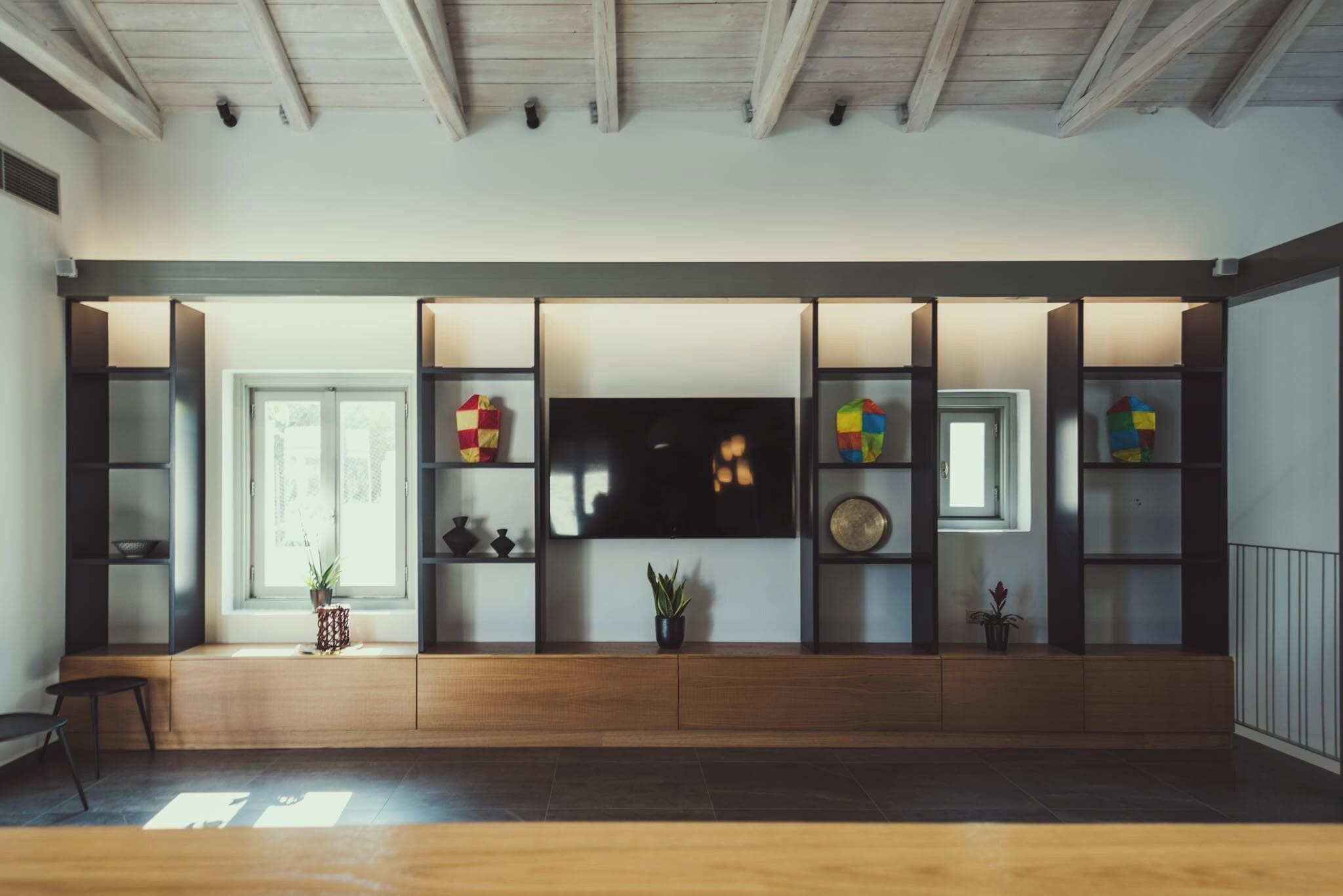 Una sala moderna con televisor integrado, estanterías de madera y una ventana.