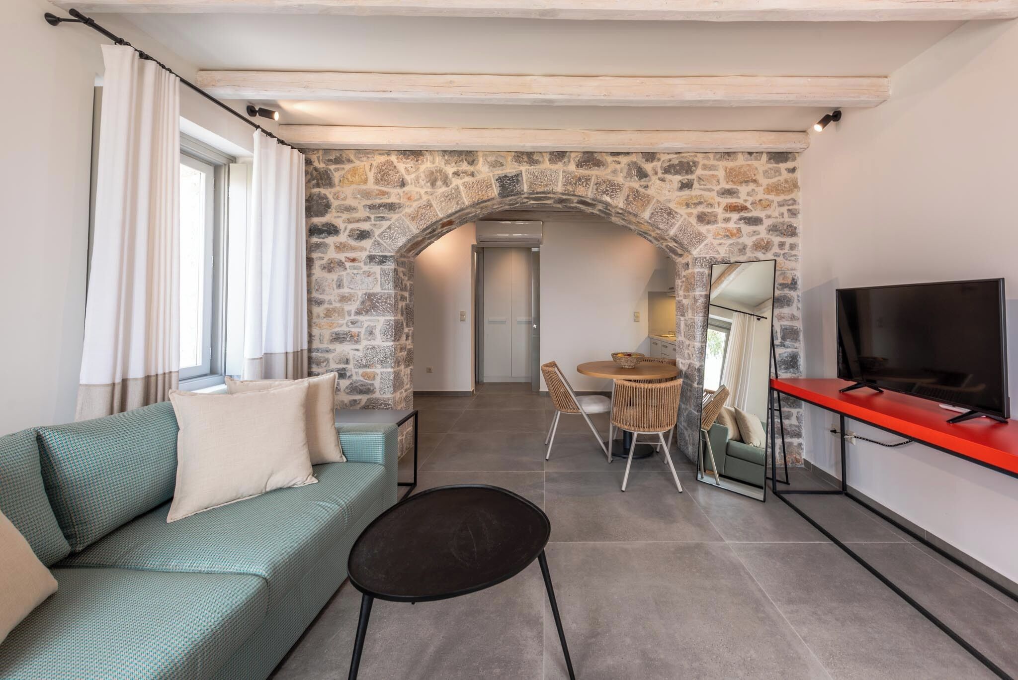 A modern living room with a stone archway, a sofa, a dining table, and a TV.