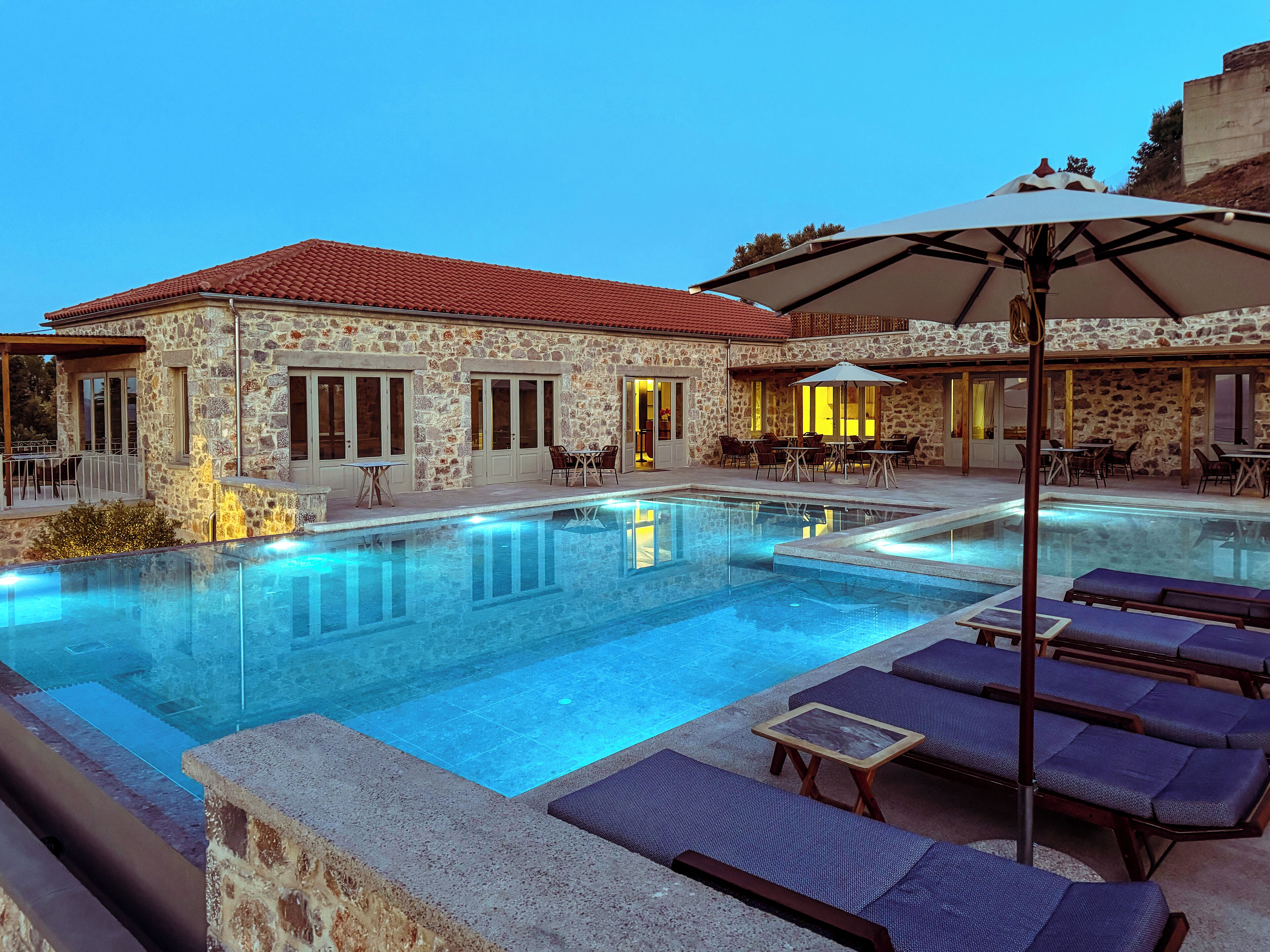 Un edificio de piedra con piscina, mobiliario exterior y sombrillas.