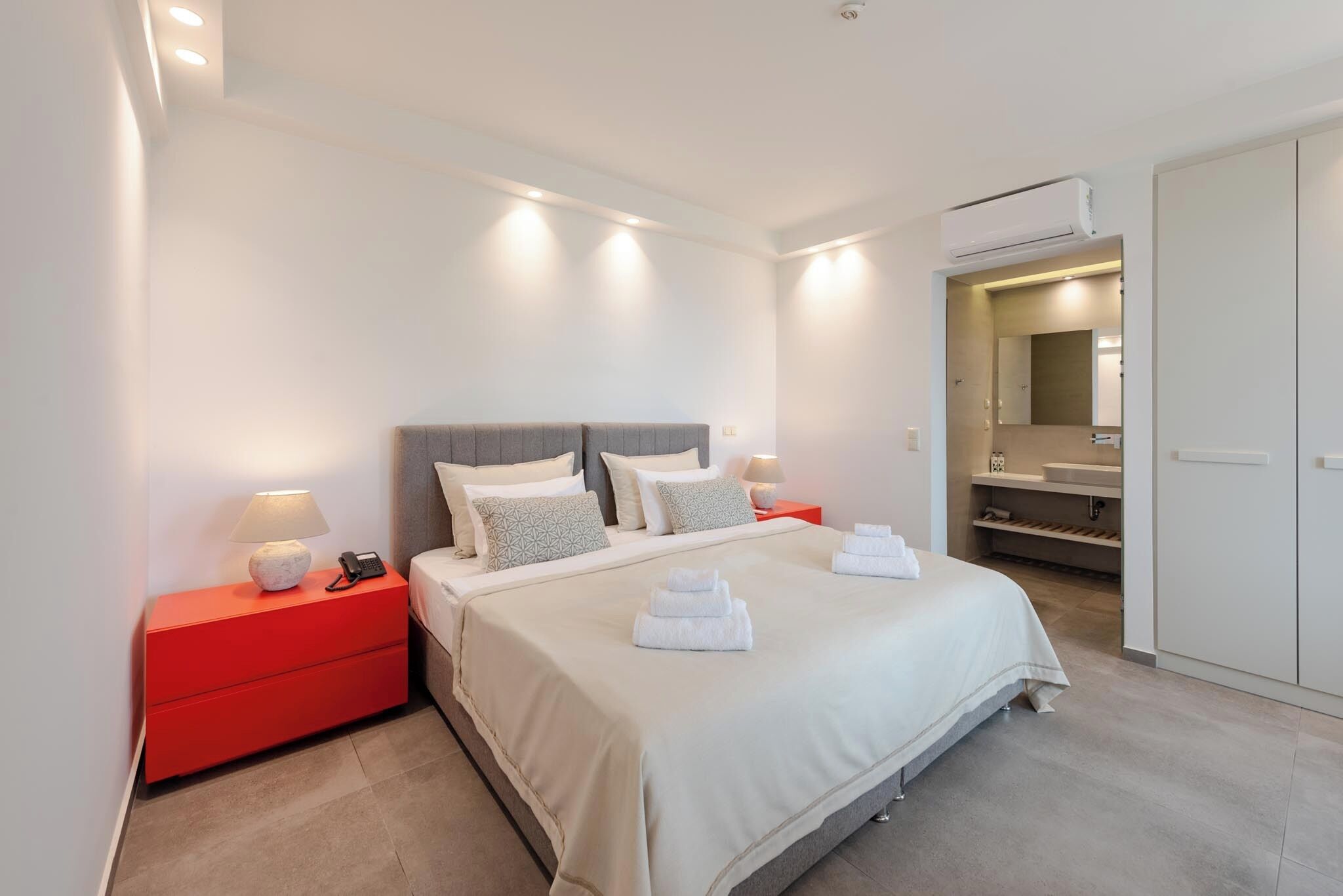 A modern hotel room with a large bed, red nightstands, a mirror, and a walk-in closet.