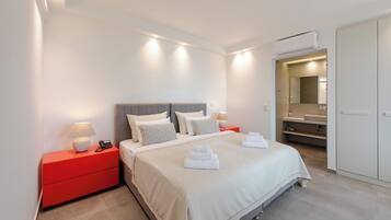 A modern hotel room with a large bed, red nightstands, a mirror, and a walk-in closet.