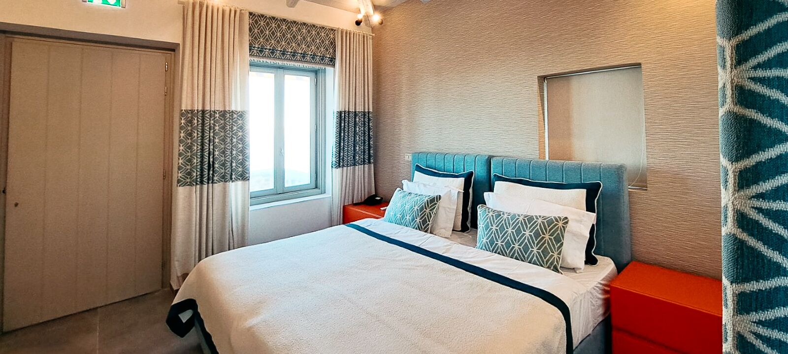 Een hotelkamer met een bed, nachtkastjes, een raam met gordijnen en een spiegel aan de muur.