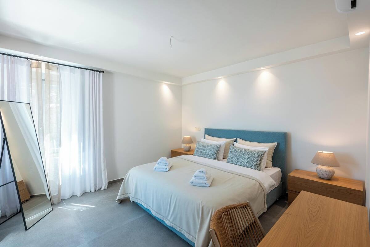 A hotel room with a bed, bedside tables, a chair, a table, and a mirror.