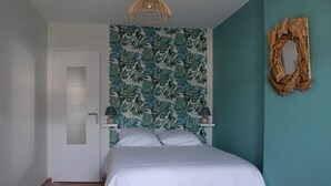 A bedroom with a bed, a door, a wall with a leaf pattern, and a wooden frame on the wall. - Gîte Padura - Location 4 Chambres - Braud et Saint Louis (Braud-et-Saint-Louis)