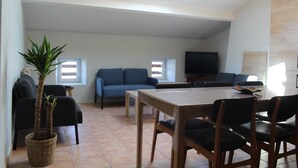 A living room with a sofa, a dining table, chairs, a television, and a potted plant. - Gîte Padura - Location 4 Chambres - Braud et Saint Louis (Braud-et-Saint-Louis)