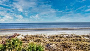 Une plage avec une promenade en bois menant au rivage, des dunes de sable et un ciel bleu dégagé.