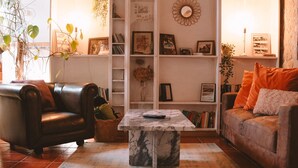 Ein gemütliches Wohnzimmer mit einem Ledersofa, einem Couchtisch und einem Bücherregal voller Bücher und Dekoration.