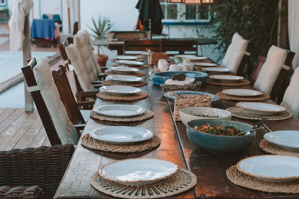 A long wooden table set for a meal with woven placemats, plates, and bowls.