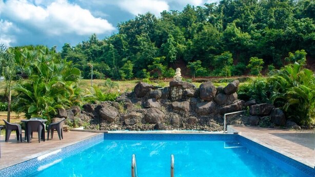 A rectangular swimming pool with a stone rock formation in the background. - Rio Forest Resort (Karjat)