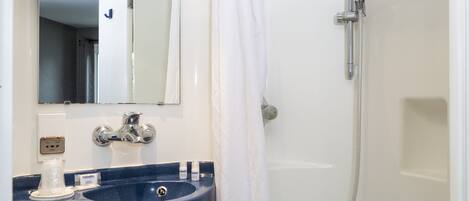 Un baño con un lavabo azul, un espejo, una ducha con cabezal de ducha manual y una cortina de ducha blanca.