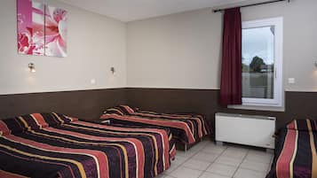 Una habitación con tres camas, un radiador, una ventana con cortinas y una lámpara fijada a la pared.