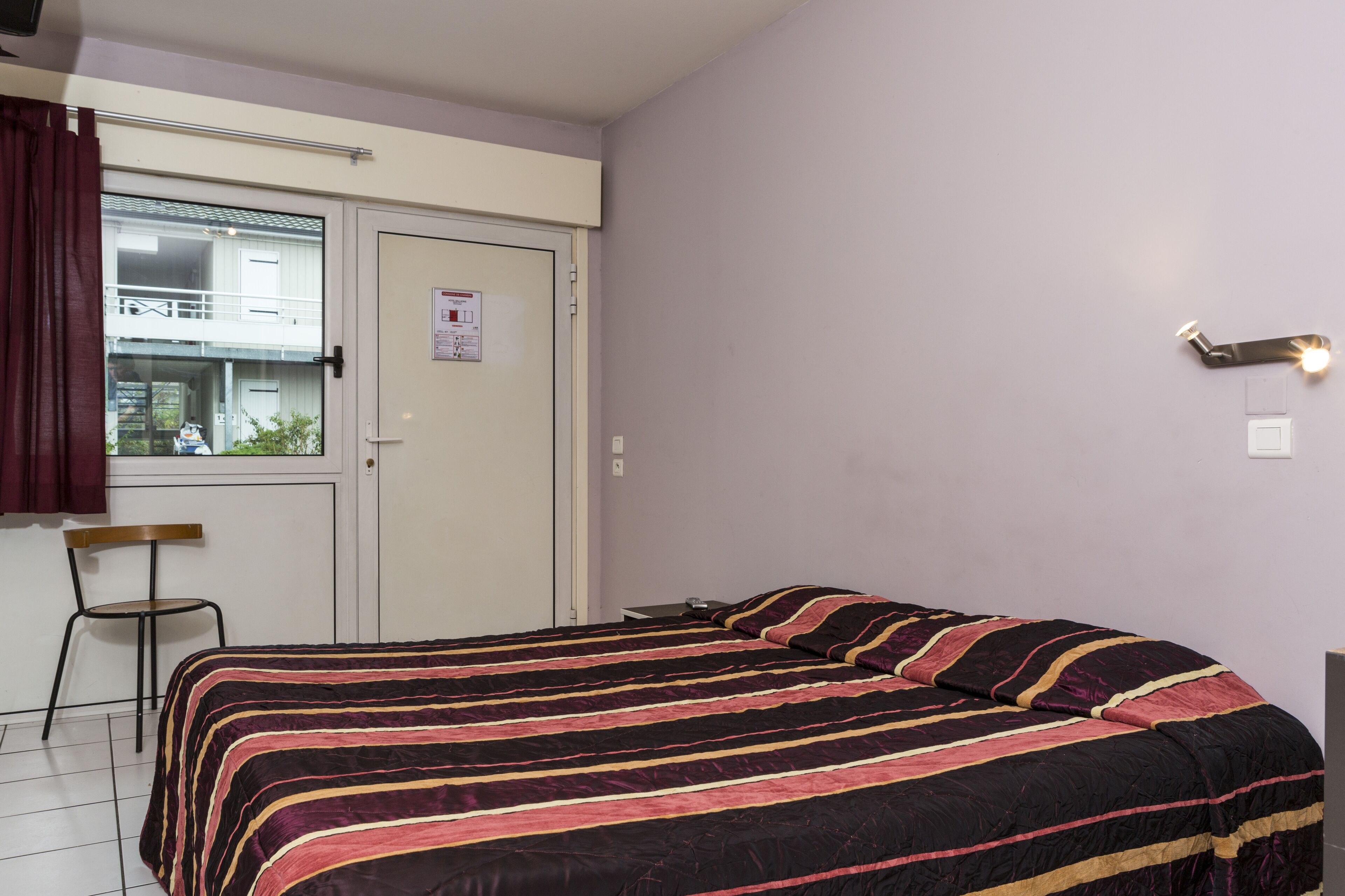 Un dormitorio con cama, una silla, un ventanal y una puerta.