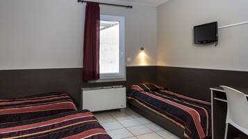 A small, well-lit room with two beds, a desk, a TV, and a window with a curtain.