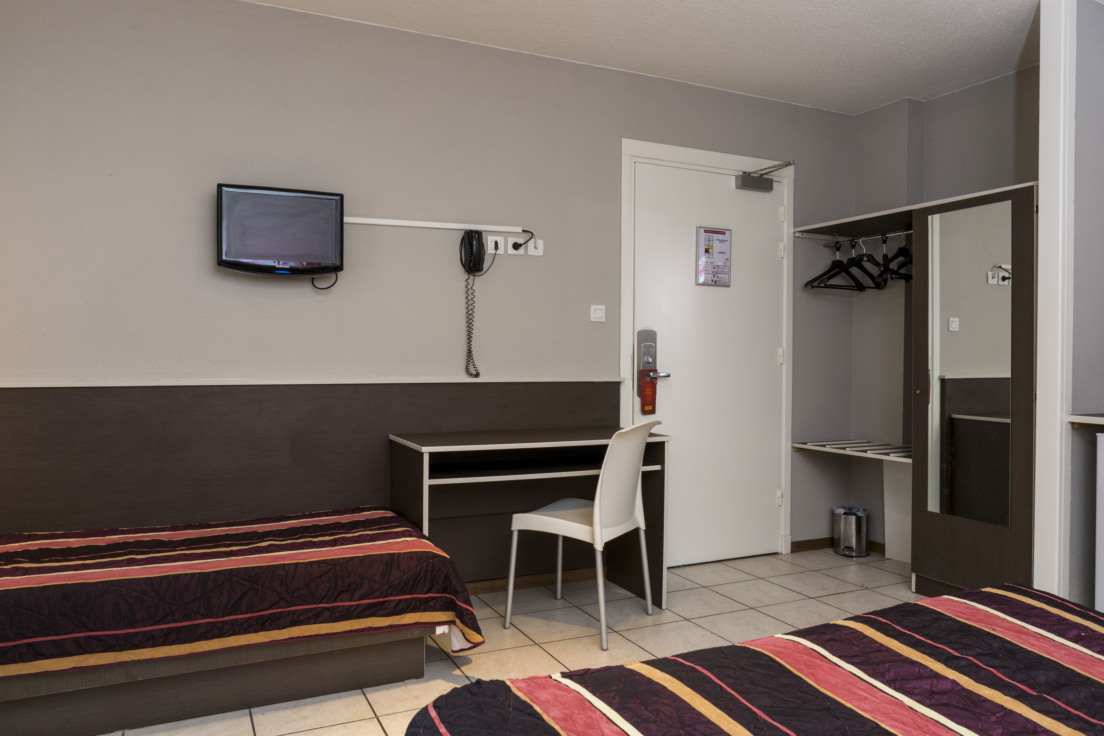 Een hotelkamer met twee bedden, een bureau, een stoel, een televisie, een telefoon en een kast.
