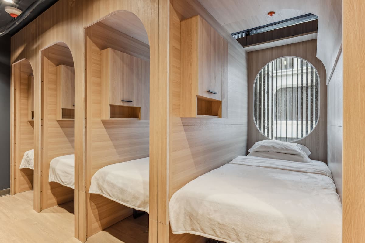 Ein Zimmer mit drei hölzernen Etagenbetten, jedes mit einer weißen Matratze und einem kleinen Regal darüber.