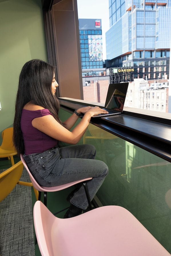 Una persona usando una computadora portátil en un asiento junto a la ventana, con vista a un paisaje urbano.