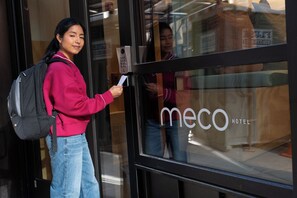 Una persona entra a un hotel con cerradura electrónica y un cartel que dice 'meco HOTEL'.