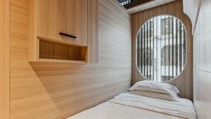 Un dormitorio moderno con cabecera de madera, ventanal circular y estante empotrado.