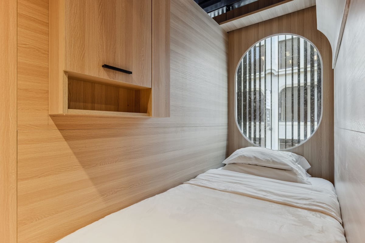 Ein modernes Schlafzimmer mit einem Holzkopfende, einem Rundfenster und einer eingebauten Ablagefläche.