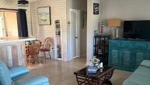 A living room with a sofa, a coffee table, and a television. There is a kitchen area with a refrigerator and a sink. - Waterfront Sea Cottage with private Pool and waterfront views (Port Charlotte)
