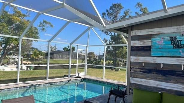 A covered swimming pool with clear blue water, surrounded by a white frame structure. There are lounge chairs and a wooden wall with a sign that reads "The Boat House". - Waterfront Sea Cottage with private Pool and waterfront views (Port Charlotte)